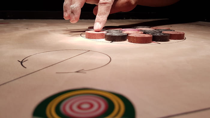 Two players deeply engrossed in a game of carrom, with the striker in motion.